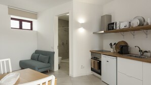 A compact kitchen with a microwave, oven, and dishwasher. There is a wooden dining table with a white chair and a grey sofa in the adjacent living area. A small window provides natural light. - Madalena Village 2 - City centre by HD PROPERTIES (Faro)