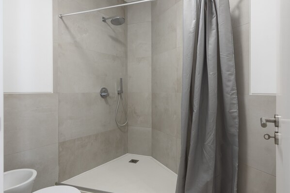 Un espace douche équipé d’un pommeau de douche, d’un pommeau de douche à main et d’un rideau.