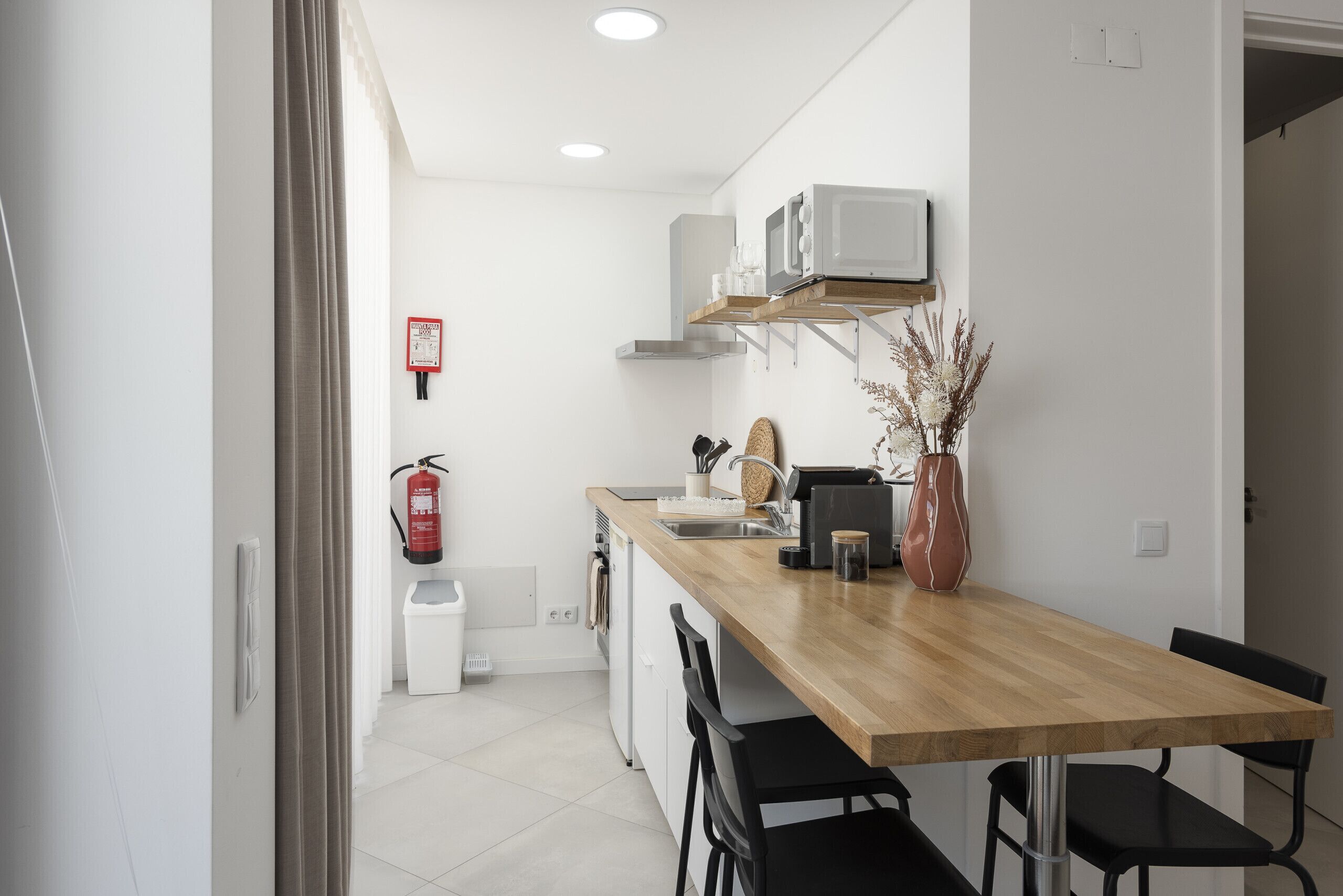 Une cuisine moderne avec un plan de travail en bois, des chaises noires et un four à micro-ondes encastré.