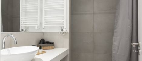 Une salle de bain moderne avec un lavabo blanc, un miroir et un espace douche.