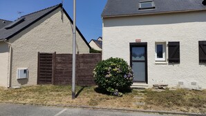 Ein zweistöckiges Haus mit Hausnummer 1060 an der Haustür, einem umzäunten Garten und einem kleinen Strauch mit violetten Blüten.