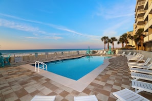A pool area with lounge chairs and a view of the ocean.