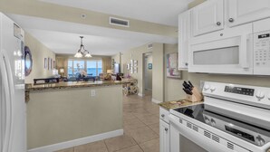A kitchen with white cabinets, a microwave, and a stove. There is a dining area with a view of the ocean. - Sandy Key 524:  2 BR / 2 BA Gulf Front Condo in Perdido Key, FL  Sleeps 6 (Pensacola)