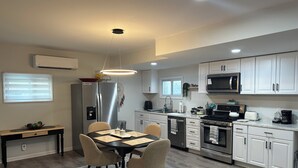 Une cuisine moderne avec des meubles blancs, des appareils en acier inoxydable, un coin repas avec une table et des chaises, et un luminaire au plafond.