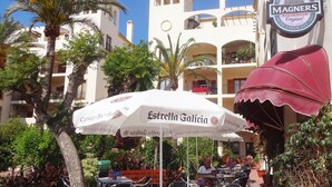 An outdoor seating area with tables and chairs, a large umbrella, and a building with balconies and a sign for 'Magners Irish Cider'. - Villa with private infinity pool close to Port (AN)