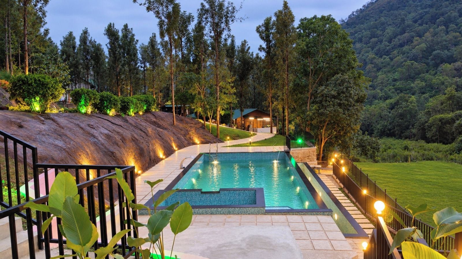 A swimming pool with a surrounding deck, a staircase, and a view of a forested hillside.