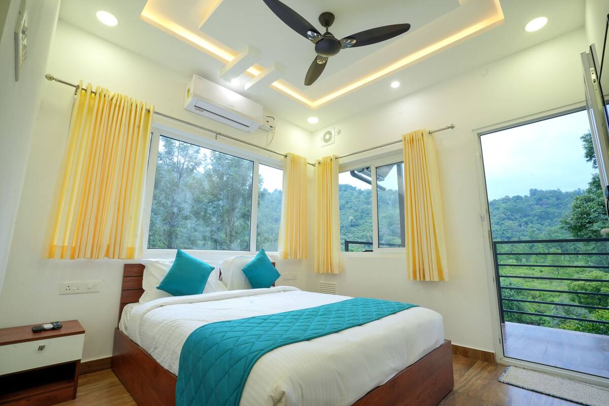 Quarto com cama, cortinas, ventilador de teto e janela com vista para o verde.