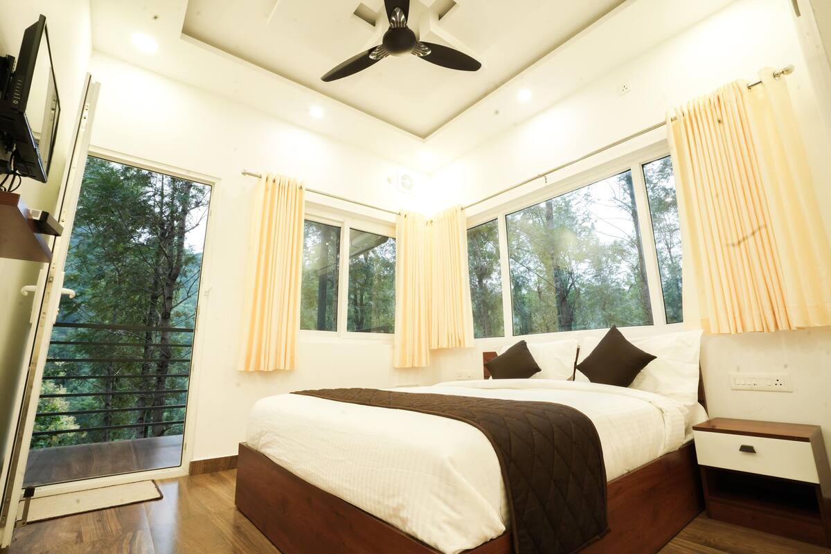 Quarto com cama grande, ventilador de teto e várias janelas com cortinas.