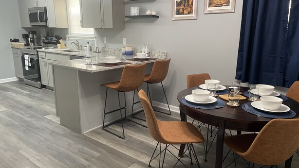 Une cuisine moderne avec des meubles gris, un micro-ondes encastré et un coin repas avec une table ronde prévue pour quatre personnes.