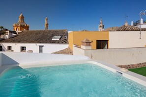 A swimming pool with a clear blue water, surrounded by buildings with white and yellow facades, and a church with a bell tower in the background. - MDD4 Health Experience Hotel Sevilla - Adults Only (Seville)