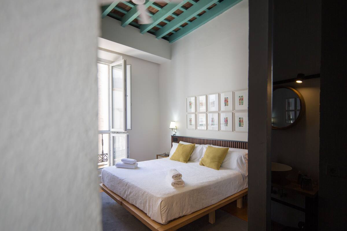 Quarto com uma cama grande, uma janela e uma parede com quadros.