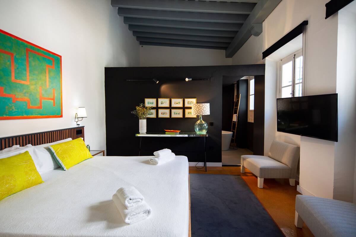 Quarto de hotel moderno com uma cama grande, uma escrivaninha, uma cadeira e uma televisão.