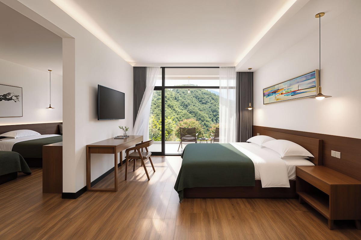 Une chambre d’hôtel équipée d’un lit, d’un bureau, de chaises, d’une télévision et d’une grande fenêtre donnant sur une zone boisée.