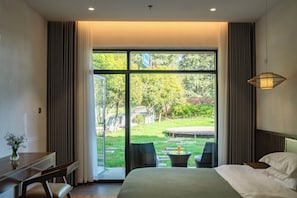 A bedroom with a large window, a bed, a desk, and a chair.