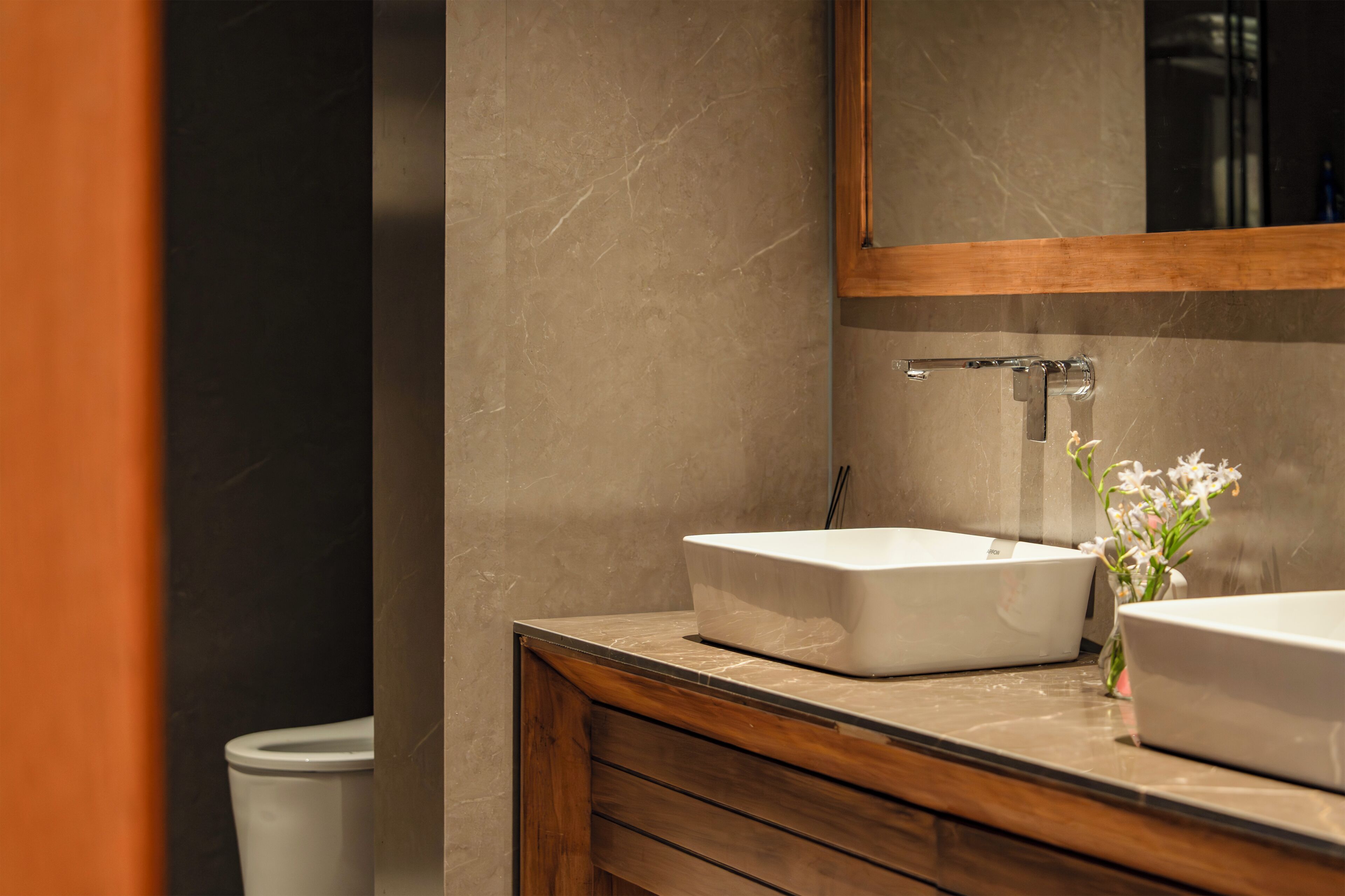 Een badkamer met een houten wastafelmeubel, twee wastafels, een spiegel en een toilet.