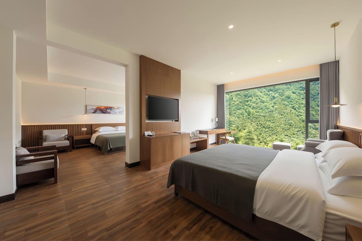 Une chambre d’hôtel moderne, dotée d’un grand lit, d’un bureau, d’une télévision et offrant une vue sur la forêt.