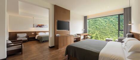 Quarto de hotel moderno com uma cama grande, uma escrivaninha, uma televisão e vista para a floresta.