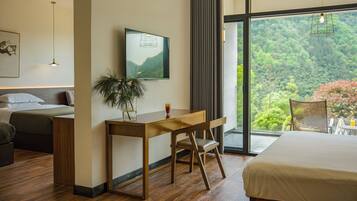 A modern hotel room with a bed, desk, and large windows offering a view of the outdoors.