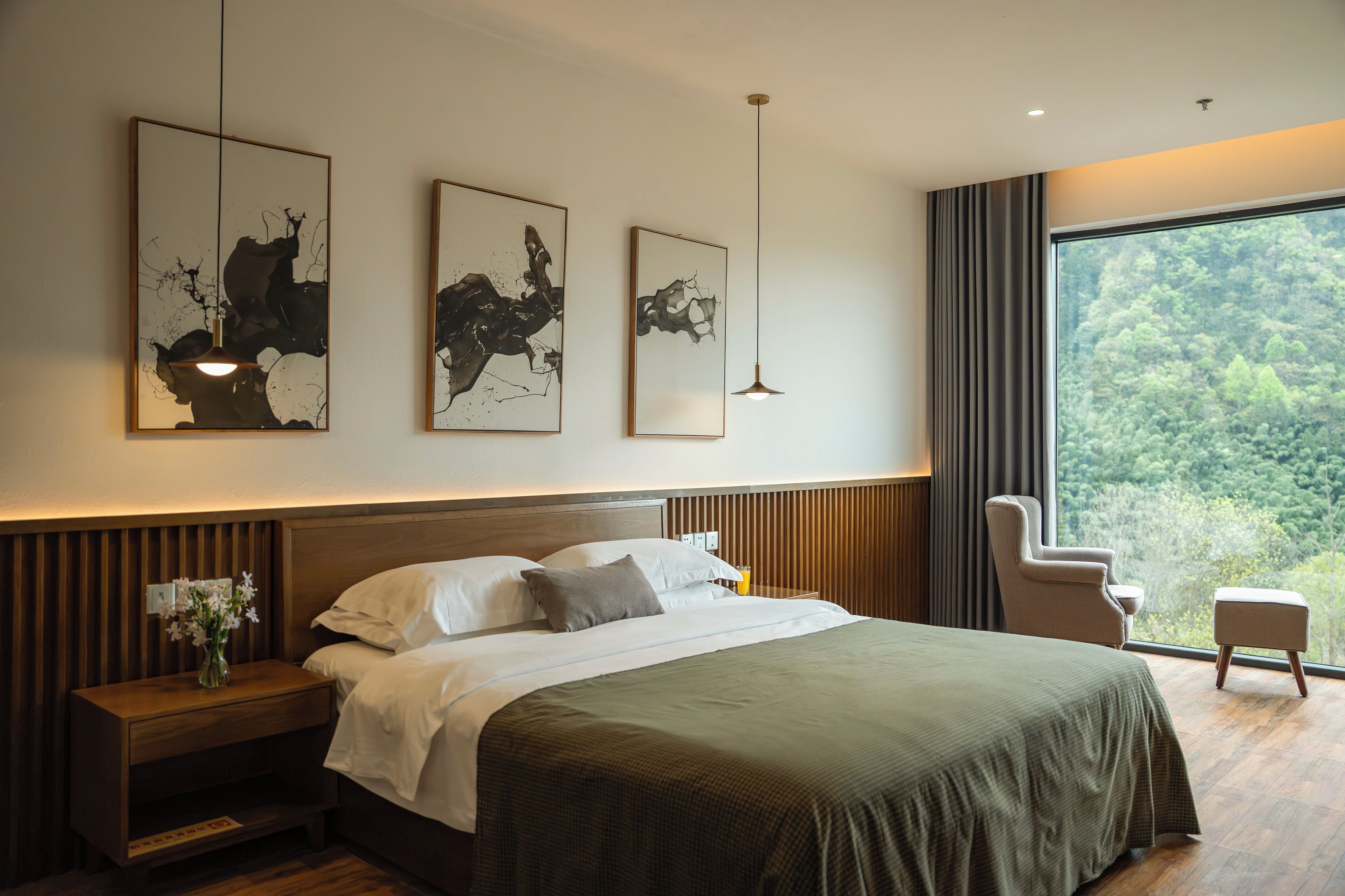 A modern hotel room with a large bed, a nightstand, a chair, and artwork on the wall.