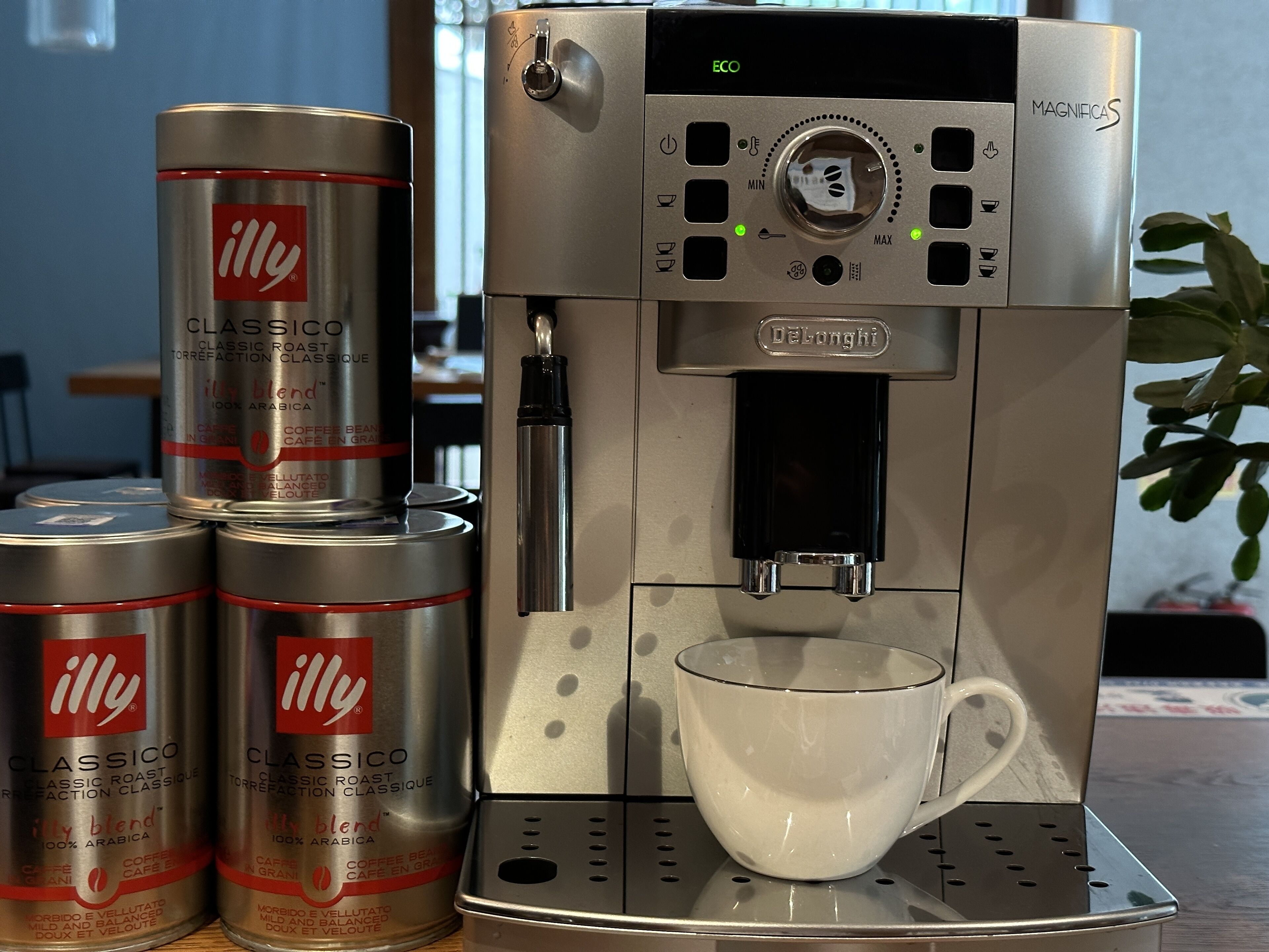 Une machine à café avec trois boîtes de café étiquetées « illy » et une tasse blanche.