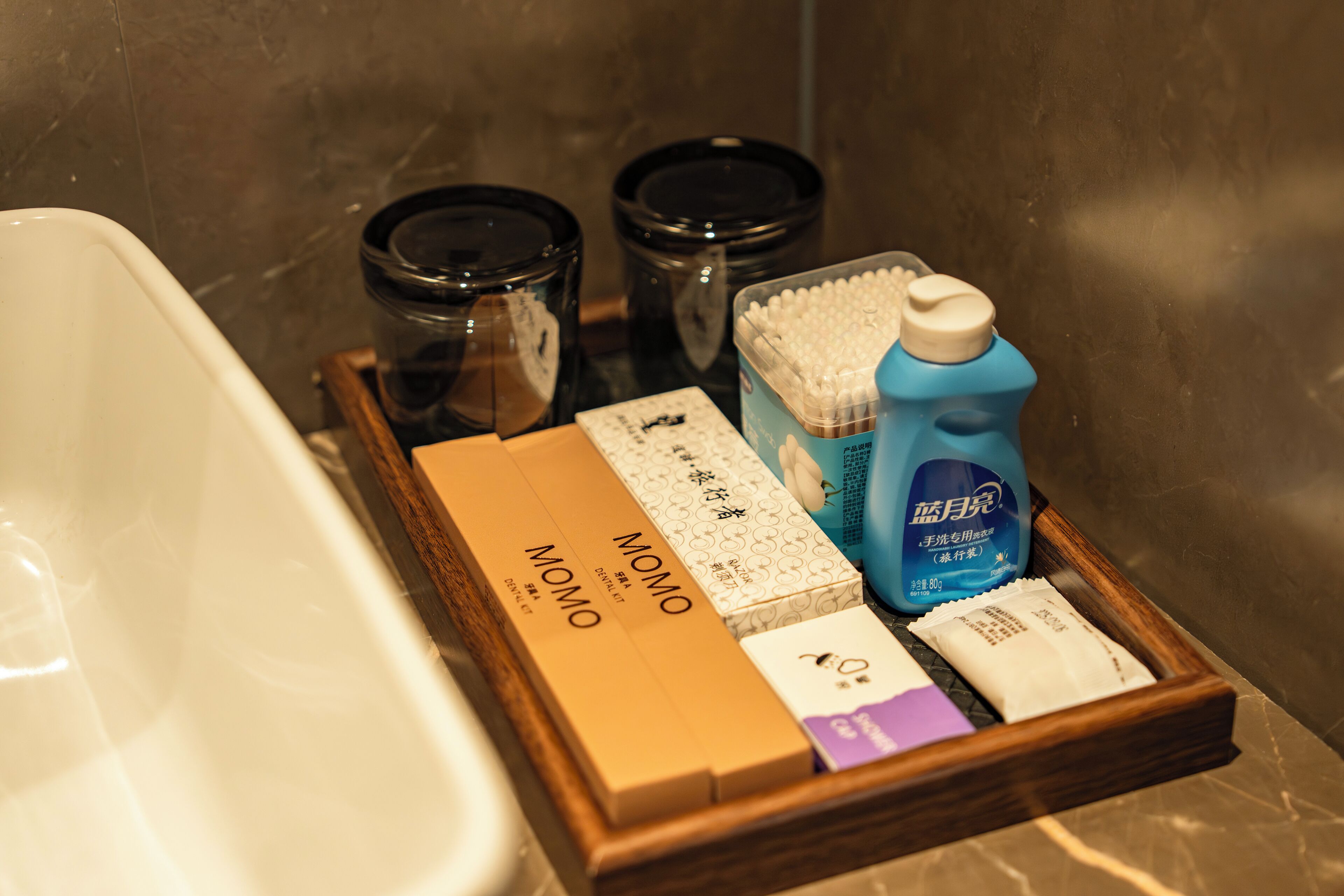 A bathroom with a bathtub, a wooden tray holding toiletries, and two black containers.