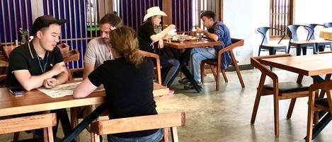 A restaurant with wooden tables and chairs, a tiled floor, and vertical blinds on the windows.