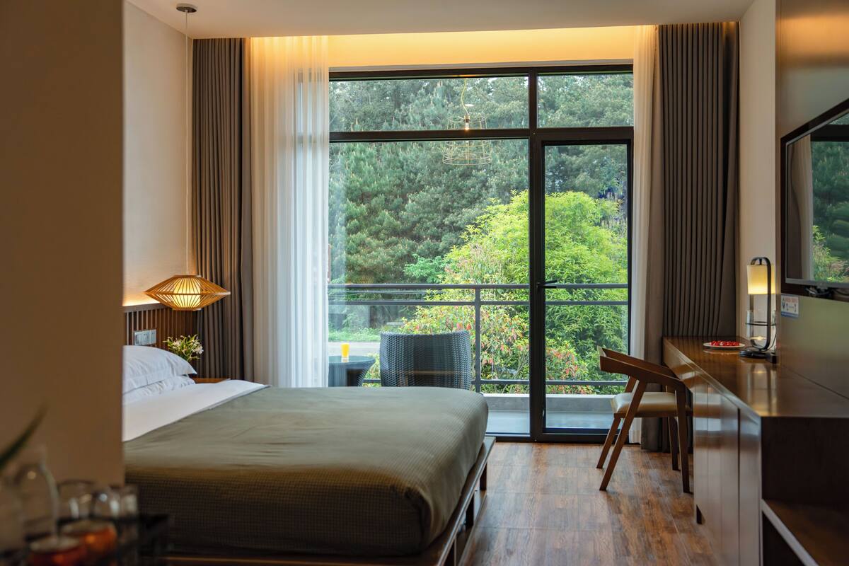 Une chambre d’hôtel équipée d’un lit, d’un bureau, d’une chaise et d’une grande fenêtre donnant sur un paysage verdoyant.