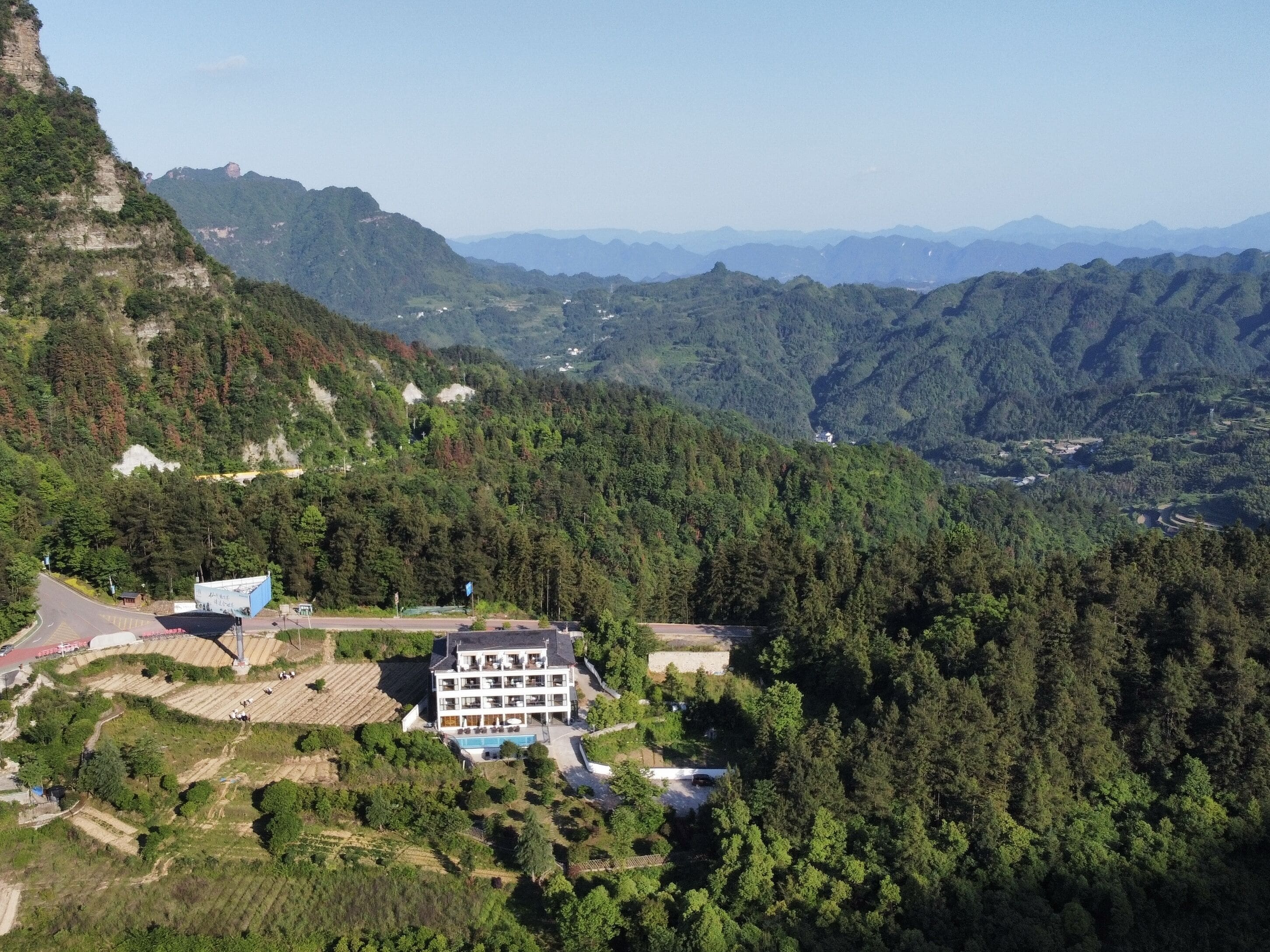 A large, multi-story hotel with a swimming pool, surrounded by lush green hills and mountains.