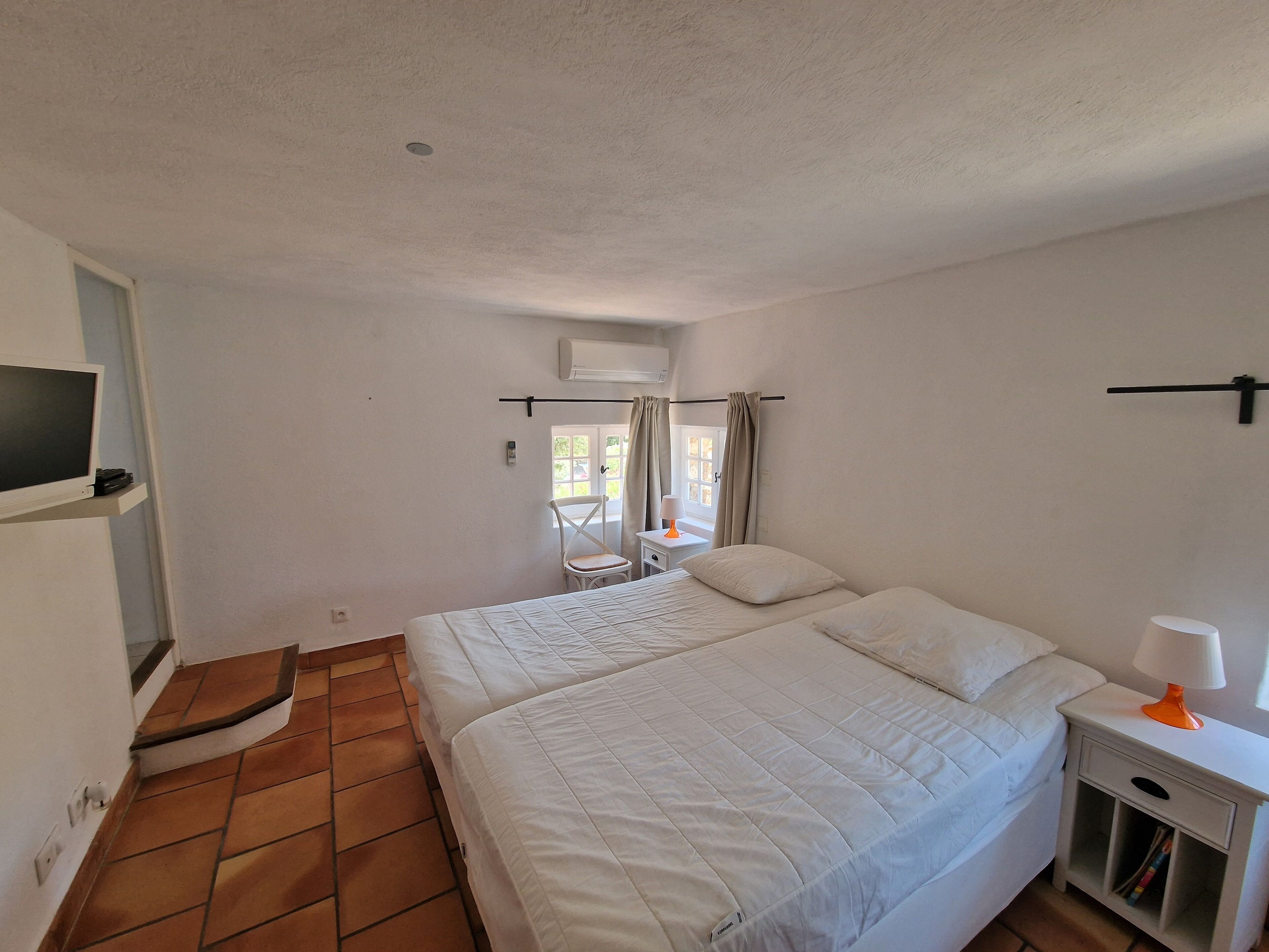 A bedroom with a bed, a chair, a nightstand, a TV, and a window with curtains.