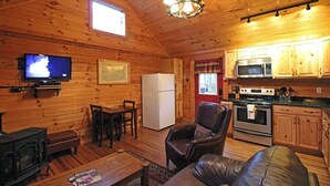 Interior acogedor de una cabaña con detalles de madera, televisión, refrigerador, microondas, horno, chimenea y asientos de cuero.