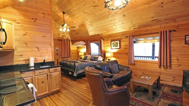 Interior acogedor de una cabaña con detalles de madera, una cama, un sofá, una mesa de comedor y una zona de cocina.