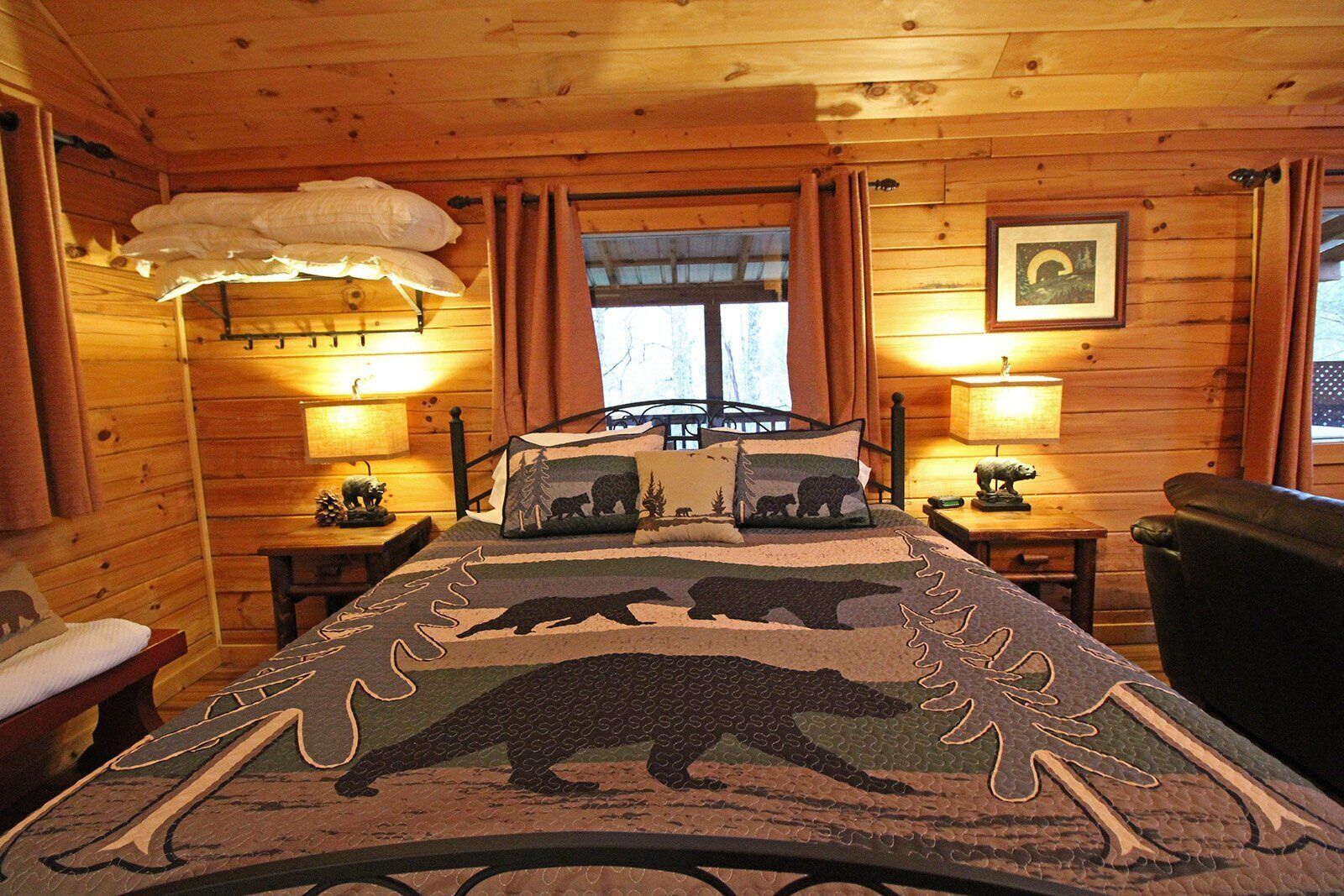 Une chambre chaleureuse dans un chalet, avec un lit agrémenté d’une courtepointe à motifs d’ours, des murs en bois et deux lampes de chevet.
