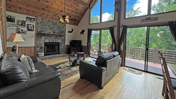 A spacious living room with a stone fireplace, leather sofas, and large windows offering a view of the outdoors.