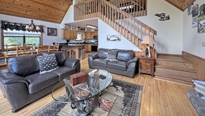 A spacious living area with a high ceiling, wooden beams, a staircase, and a kitchen.