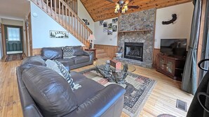 A cozy living room with a stone fireplace, leather sofa, and a staircase leading to an upper level.