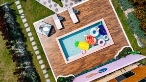 En vy från ovan över ett poolområde med solstolar, en pool och en rund sittgrupp.