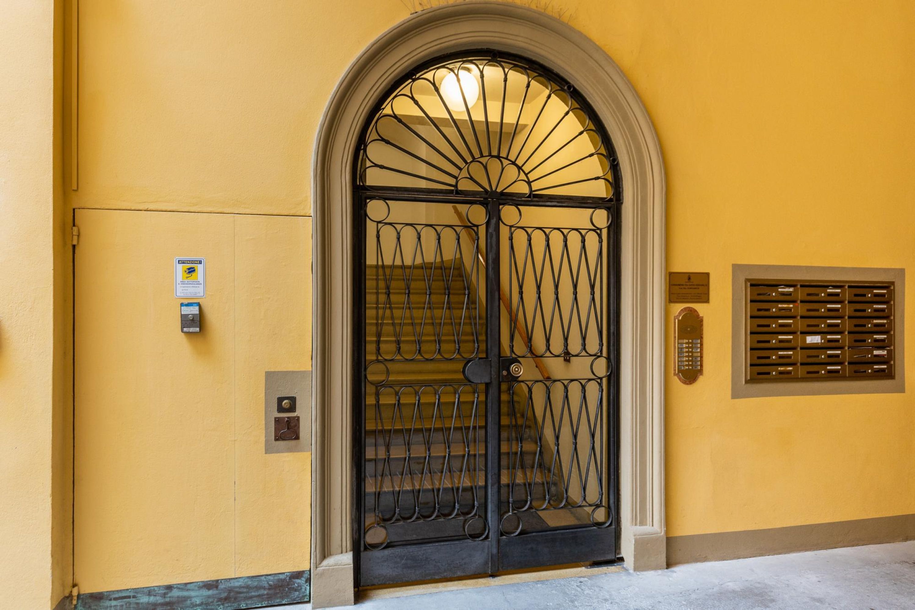 Un bâtiment jaune avec un portail en fer noir et une fente pour le courrier.