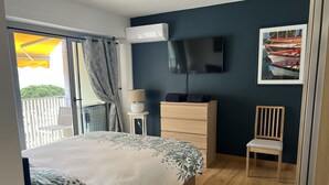 Un dormitorio con cama, cómoda, silla, televisión y balcón con vistas.