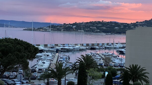 Una marina con barcos amarrados, un aparcamiento y un paisaje montañoso al fondo.