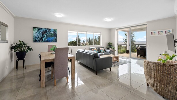 Amplia sala de estar con sofá, mesa de comedor y sillas, ventanas grandes con vistas al exterior.