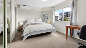 Un dormitorio con cama, mesitas de noche, escritorio y ventana con vistas a edificios.