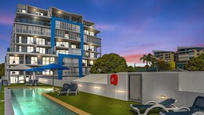 Un hotel moderno con piscina, sillones de descanso y un carretel de manguera contra incendios.