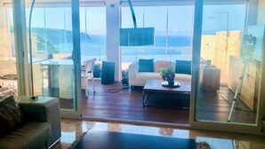 Een moderne woonkamer met een grote glazen schuifpui die uitkomt op een balkon met uitzicht op zee.