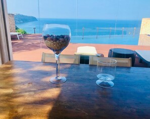 A table with a glass of nuts and a clear glass, overlooking a coastal view with a stone wall and a bench. - Villa Pareada con Piscina Infinity e Incomparables Vistas (Puigderrós)