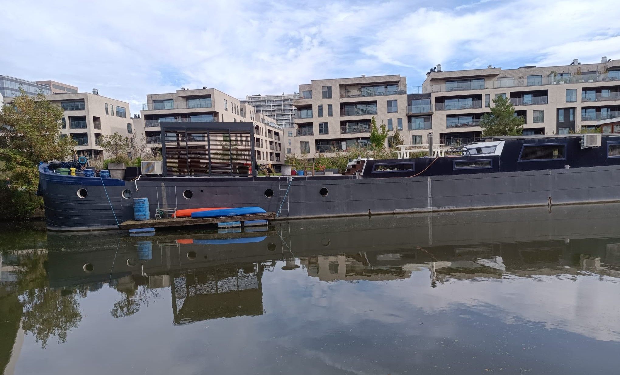 A waterfront property with a dock, a boat, and modern buildings in the background.