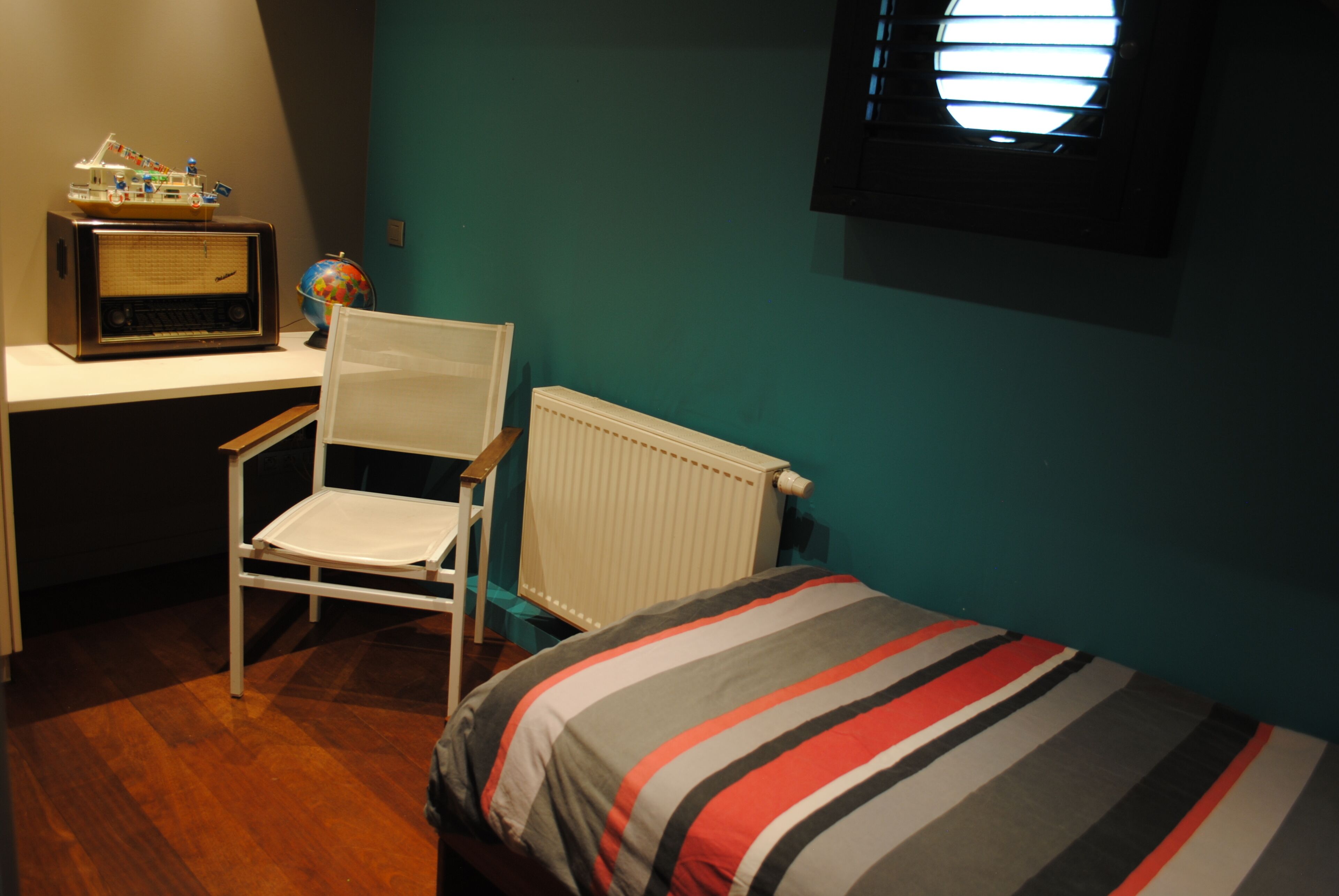 A bedroom with a bed, a desk with a radio, a globe, and a chair.