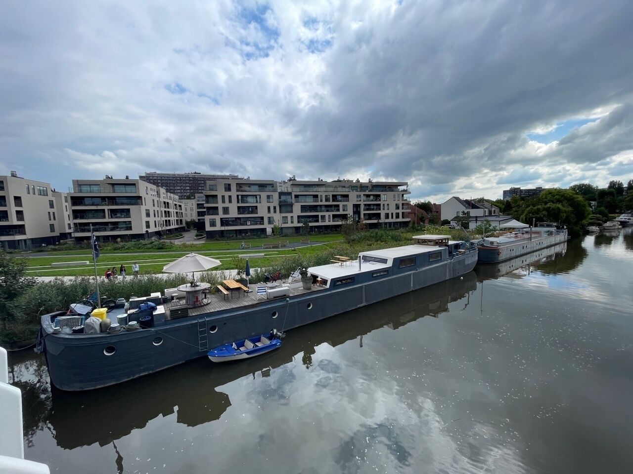 A large riverboat docked at a marina with modern buildings in the background.