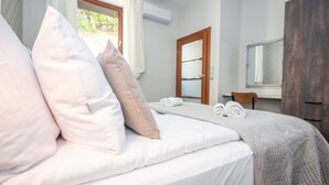 Un lit bien fait, avec des oreillers, une chaise en bois, un miroir et une fenêtre avec des rideaux.