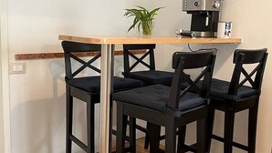 A small dining area with a wooden table and four black chairs. There is a coffee machine on the table and a potted plant on the left side. - At home in Oltrearno (Firenze)