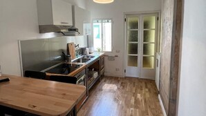 A modern kitchen with a wooden table and chairs, a hanging light fixture, and a view of a room with a door and windows. - At home in Oltrearno (Firenze)